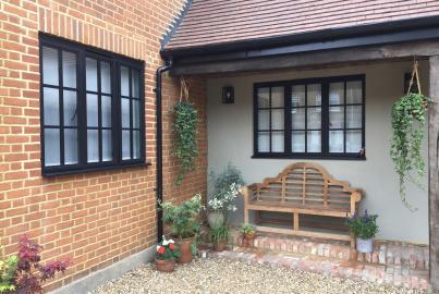 Black steel-replacement windows with grid panes, on a brick house patio with a wooden bench