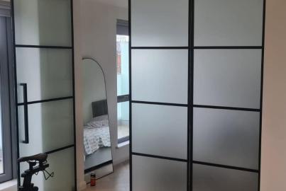 Black steel-look screen with frosted glass panels and a mirrored section, used as a room divider in a bedroom with an exercise bike