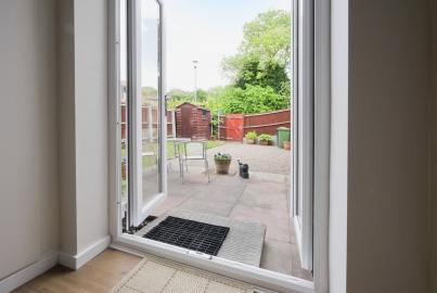 View from inside through an open white Alitherm double door, looking out onto a patio and garden with a shed