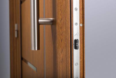 Close-up of the multi-point locking mechanism and vertical handle on the side of an open, wood-effect Origin front door