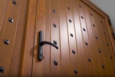 Close-up of a traditional wood-effect Origin front door with vertical panels, a black lever handle, and decorative black studs