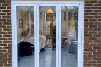 Exterior view of closed, white three-panel Origin OB-49 bifold doors installed in a brick conservatory