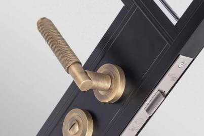 Detailed close-up of a knurled bronze lever handle and thumb-turn lock on a black Origin OI-30 door