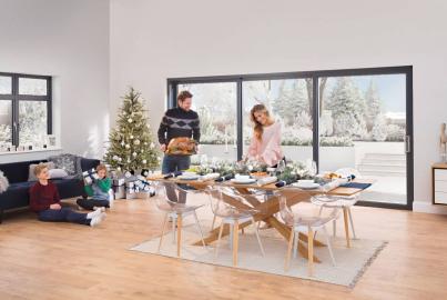 Family setting a Christmas table in a dining room with a large black Origin OS-77 sliding door showing a snowy garden