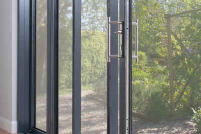 Close-up of a dark grey Origin OS-77 sliding door on a wood floor, showing the stainless steel handle and view of a garden