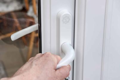 Close-up of a hand turning the white lever handle to open a white Alitherm door