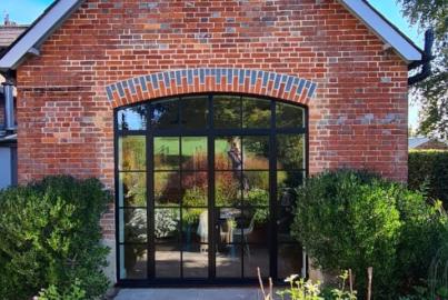 Exterior view of a red brick building with the black steel-look arched doors fully closed. A sunny patio is in the foreground
