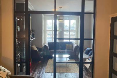 A black steel-replacement internal screen and doorway separating two living rooms. A sofa is visible in the far room.
