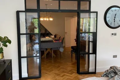 Fully open black Aluco steel-look double doors with a top panel, connecting a living room to a dining area