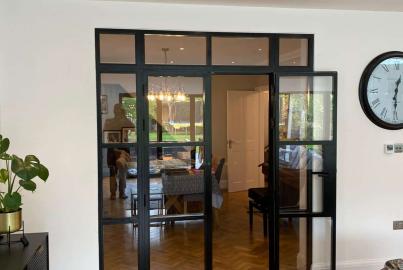 Black Aluco steel-look double doors with one door open, viewed from a living room with herringbone floors