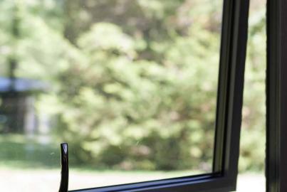 Close-up of an open, dark-framed casement window with a black handle, showing a blurred green garden outside