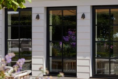 Three tall, black steel-replacement windows with grid patterns, set into a white clad house exterior