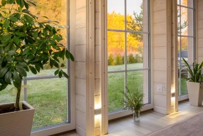 A bright room with white wood walls and large, white aluminium windows with a grid pattern, looking out onto a sunny field