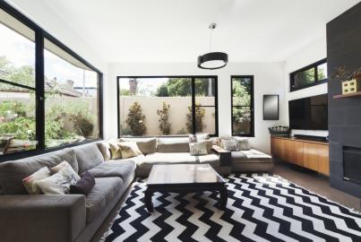 Modern living room with a large grey sofa, chevron rug, and black-framed windows looking onto a patio