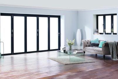 Minimalist living room with dark grey five-panel Origin bifold doors and a matching three-panel Origin window