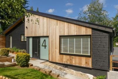 A modern house with black and wood cladding, featuring a wide, black-framed aluminium window with blinds