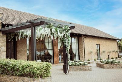 Brick venue exterior with a black pergola. Large, black steel-replacement windows and doors are visible