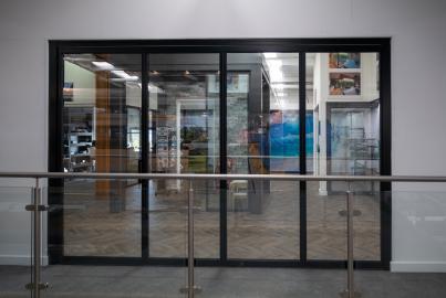 A large black slimline patio door with multiple panels, seen from across a glass balustrade in a showroom