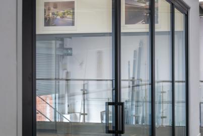 Angled view of a closed black slimline sliding door in a showroom, showing the modern vertical handle