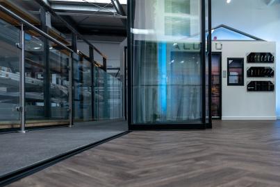 Angled view of a closed black slimline sliding door in a showroom, showing the modern vertical handle
