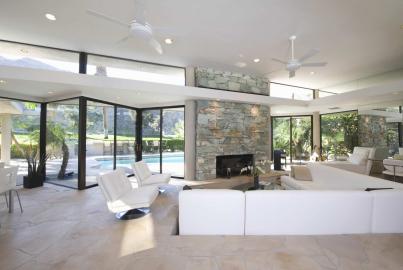 Modern living room with a stone fireplace, white sofas, and large black sliding doors open to a pool