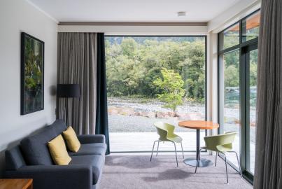 A modern room with a grey sofa and a large, dark-framed sliding glass door and corner window looking out onto a river.