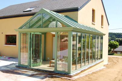 A glass conservatory with a pale green Alitherm double door open, attached to a yellow house