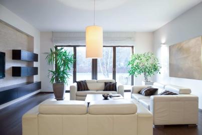 A modern living room with white leather sofas and dark-framed double doors in the background leading to a garden.