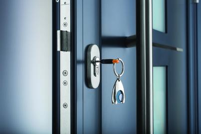 Close-up of a key in the lock of a dark blue Origin front door, showing the vertical handle and high-security locking strip