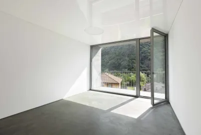 Empty, minimalist room with a concrete floor. A single grey Alitherm door is open, leading to a balcony with a mountain view