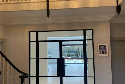 Black Aluco steel-look doors and side panel in a grand hallway with a curved staircase and white tiled floor
