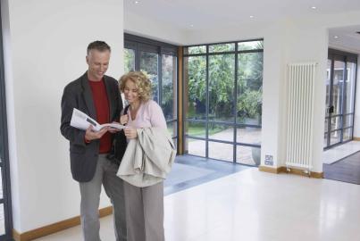 Couple smiling and looking at a brochure in a modern room with large, black steel-look windows in the background