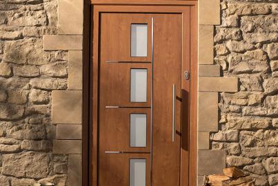Wood-effect front door with four frosted glass panels and a vertical handle. Set in a rustic stone wall with boots and logs outside