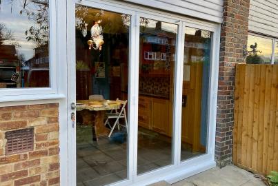 Exterior view of closed white three-panel Origin OB-49 bifold doors, with a kitchen interior reflected in the glass
