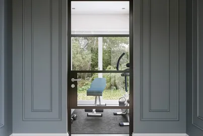 A single black Origin OI-30 internal door with a mid-rail, set in a grey panelled wall and leading into a home gym