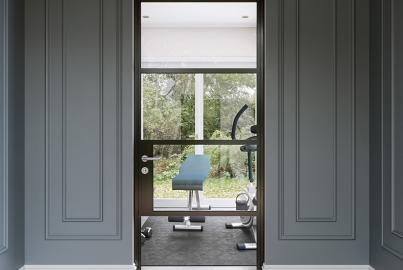A single black Origin OI-30 internal door with a mid-rail, set in a grey panelled wall and leading into a home gym