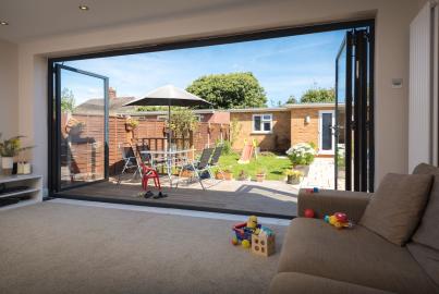 Dark grey Origin OB-49 bifold doors partially open, viewed from a living room, looking out onto a sunny garden deck