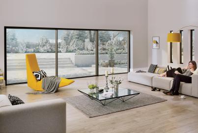 Couple relaxing on a sofa in a modern living room with large Origin sliding doors looking out onto a snowy garden