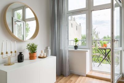 Bright room with a white cabinet and mirror. A single white Alitherm door stands open, leading to a small furnished balcony