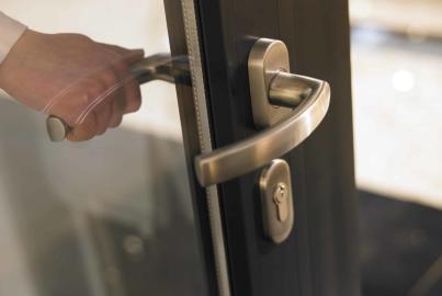 Close-up of a hand turning the brushed metal lever handle on a dark grey Origin double door