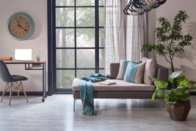 A modern living room with a chaise lounge and a large black steel-replacement window with a grid pattern, looking out to a forest