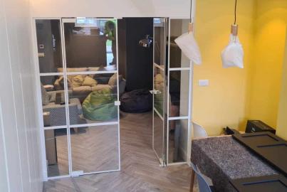 Open white steel-look doors with mirrored glass, leading from an unfinished room with a yellow wall into a modern living area