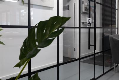A black steel-look glass door with a grid pattern, vertical handle, and 'PULL' sticker, next to a grey armchair in an office