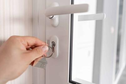 A hand inserts a key with a house-shaped keyring into the lock of a white Alitherm single door