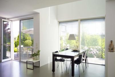 Modern dining room with large windows and a white Origin double door open to a sunny patio and garden