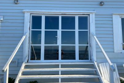 Exterior view of a closed white steel-look bifold door set, at the top of white stairs on a blue clad building